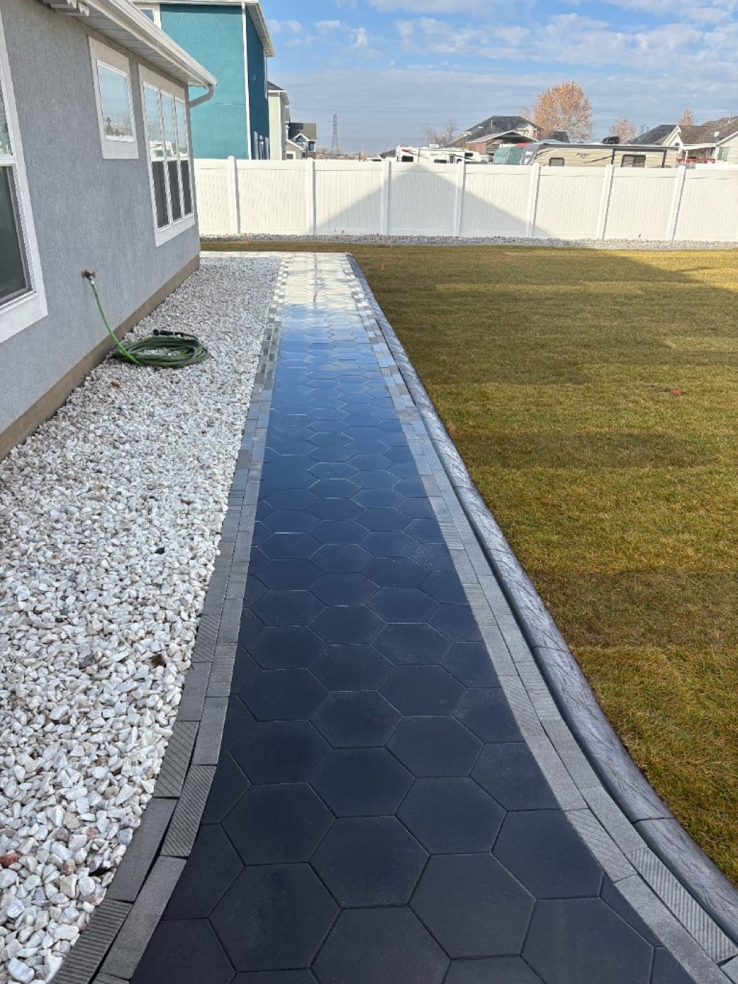 Completed charcoal hexagonal paver walkway with white rock border in a Utah backyard
