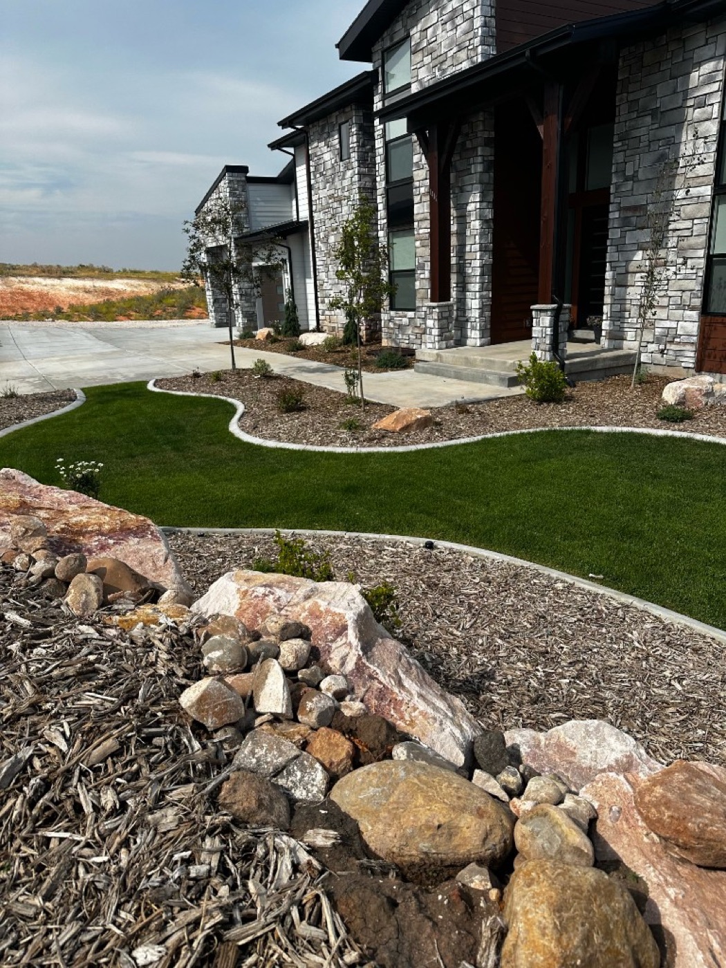 Stone home exterior in Utah with decorative concrete curbing bordering mulch beds